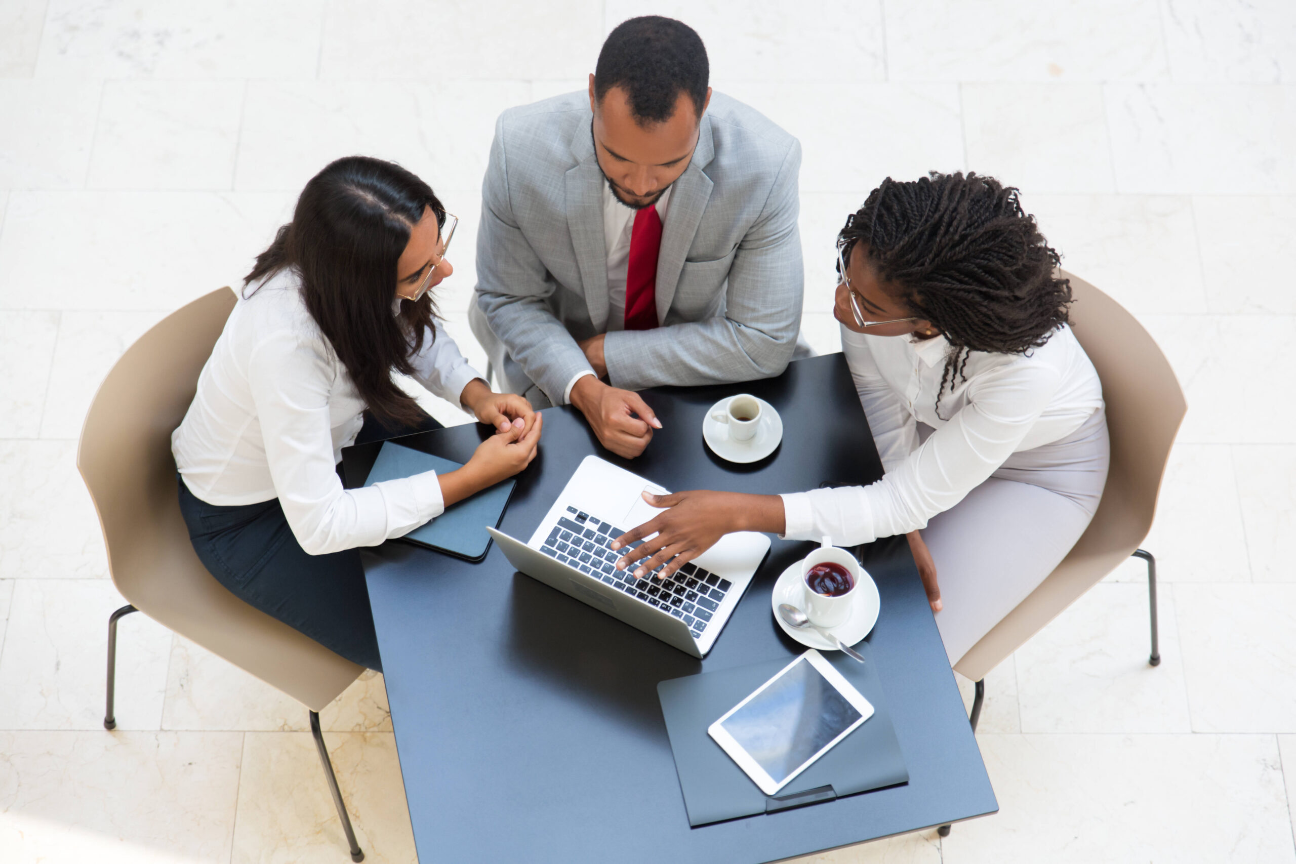 Business team working on laptop during coffee break. Business man and women sitting at table with tablet and cups, using computer and talking. Digital communication concept.